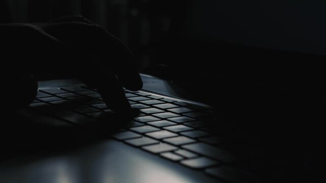 Close up silhouette of hand typing on laptop keyboard in low light during night computer work
