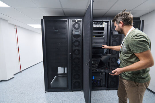 IT technician inspecting server racks with laptop in a secure data center server room