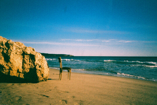 a wooden chair facing the sea on an empty beach, 35mm film