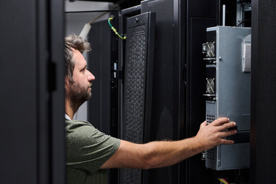 IT technician installing server hardware in a data center rack performing maintenance and inspection