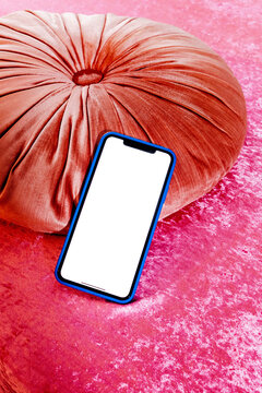 a blank screen smartphone beside a round velvet cushion