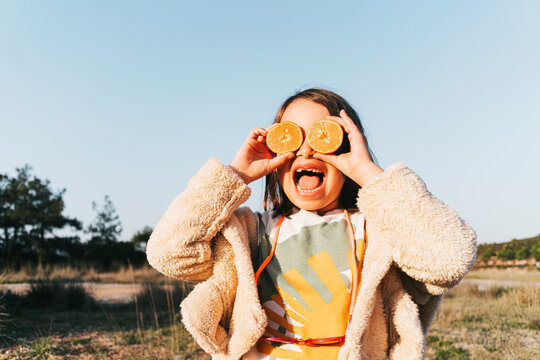 Little girl holding oranges over her eyes