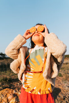 Little girl holding oranges over her eyes