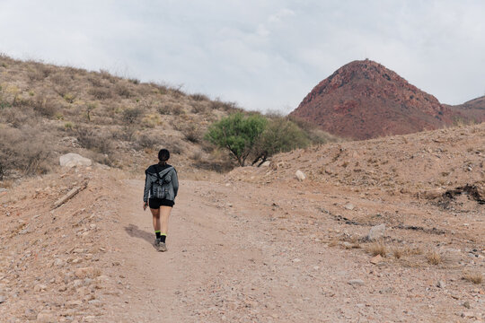Woman walking along desert path towards reddish mountain.