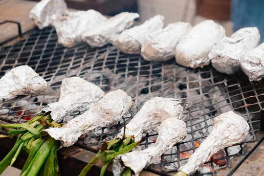 Food wrapped in aluminum foil on a charcoal grill.