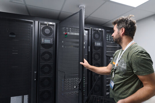 IT technician inspecting server racks in a data center with network equipment and monitoring console