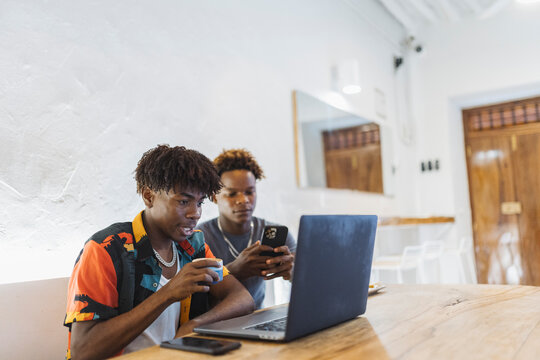 Young men enjoying coffee, using laptop and smartphone