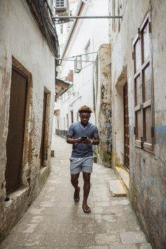 Young man walking and using smartphone in Stone Town alley
