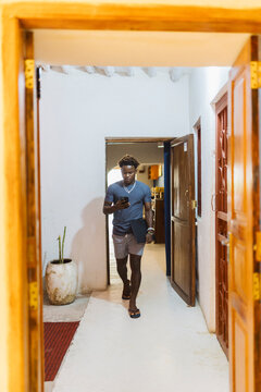 Young black man walking through corridor using smartphone