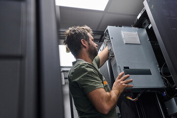 IT technician installing server hardware in a data center rack performing maintenance and network...
