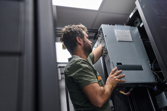 IT technician installing server hardware in a data center rack performing maintenance and network setup