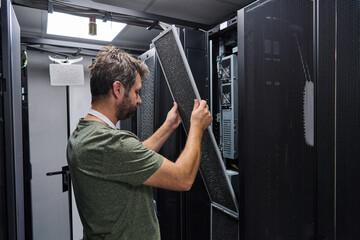 IT technician replacing air filter panel in a server room rack during data center maintenance and...