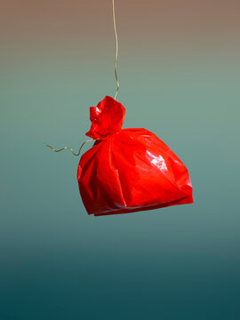 Red plastic bag suspended in mid-air against a gradient background.