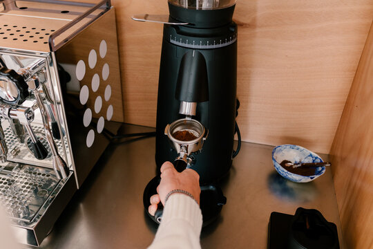 Unidentified man&rsquo;s hand holding a coffee filter under a modern grinder