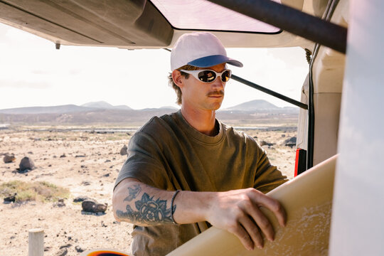 Surfer retrieving his surfboard from the open trunk of a van