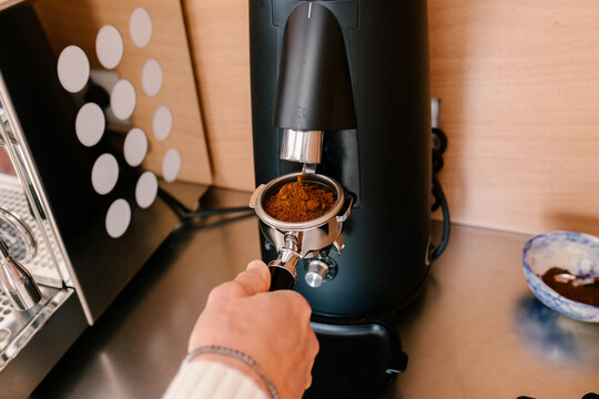 Man's hand holding a filter holder beneath a modern coffee grinder