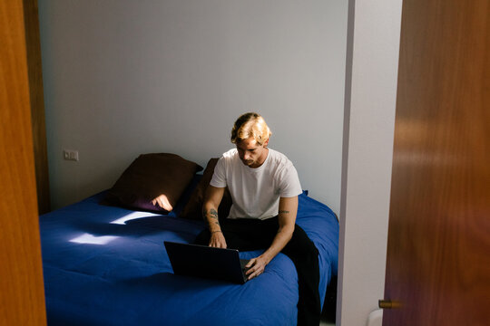 Young man working remotely on a laptop in a minimalist bedroom
