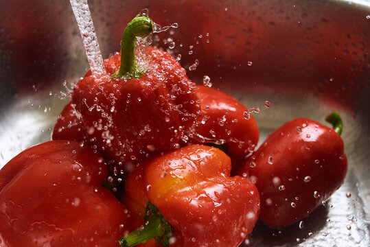 Washing red bell peppers in a sink with water