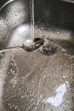 Water flows over a spoon in a kitchen sink