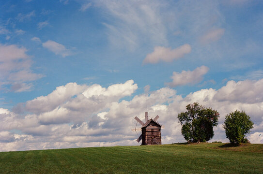 Old windmill on green hill under clouds 
