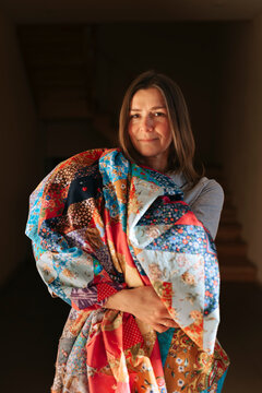 Woman Holding a Colorful Quilt in a Cozy Indoor Setting