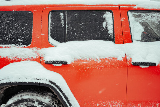 Snow covers orange vehicle parked in winter