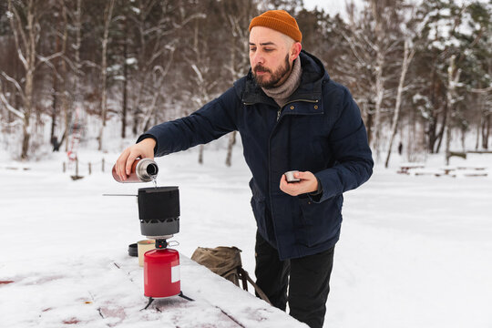 Man preparing hot coffee with camping stove in winter snow