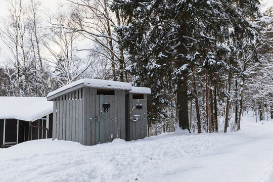 Small wooden outdoor toilet cabin in a snowy winter forest