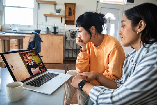 Two women in kitchen watching online consultation on laptop