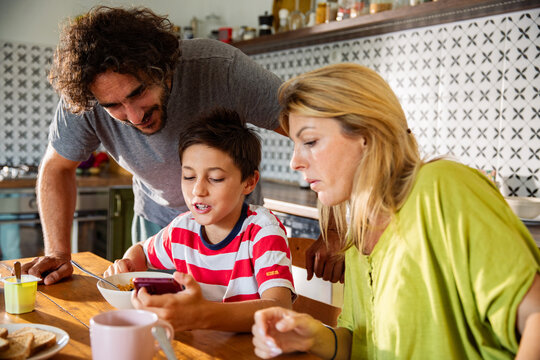 Parents and son using smartphone at breakfast table in kitchen