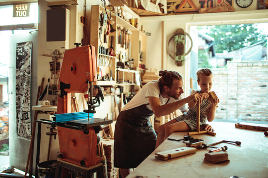 Father teaching child woodworking in home workshop