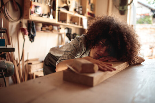 Tired woodworker resting on workbench in carpentry workshop