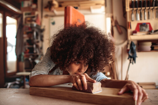Young woodworker sanding wooden board in home workshop