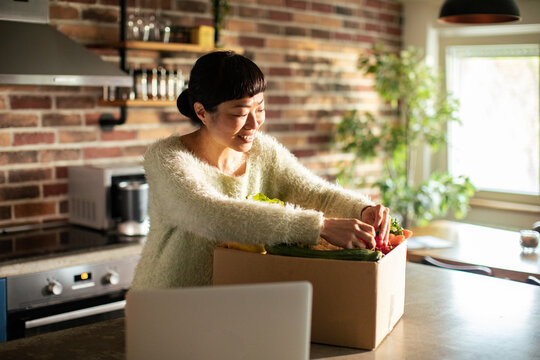 Smiling woman unboxing fresh groceries in home kitchen