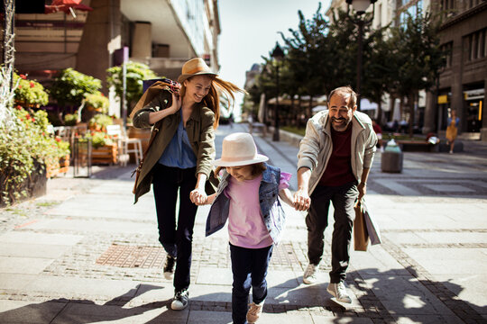 Parents and daughter running on city shopping street
