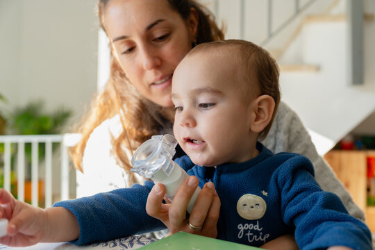 Mother assisting toddler using inhaler for asthma treatment
