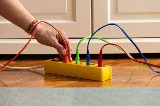 Hand Plugging Colorful Cord into Power Strip on Wooden Floor