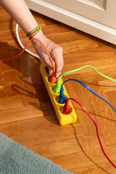 Hand Plugging Colorful Cord into Power Strip on Wooden Floor