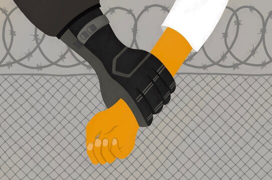 A uniformed gloved grips a prisoner with barbed fencing.