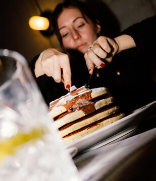 Woman using cutlery to eat a plate of pancakes with chocolate