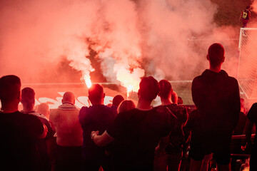 Crowd cheers during night soccer match with flares