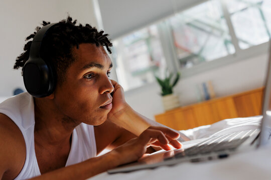 Man with dreadlocks working on laptop in bed