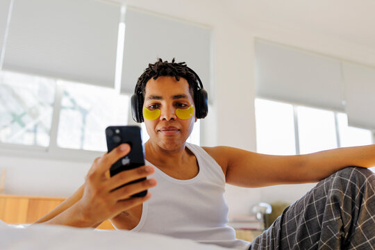 Man doing self care routine with eye patches and using phone