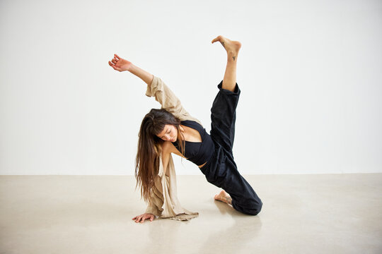 Dancer performs dynamic pose on a plain studio floor during dayt