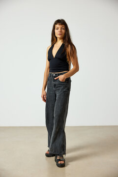 Woman in black top and wide jeans stands in studio space