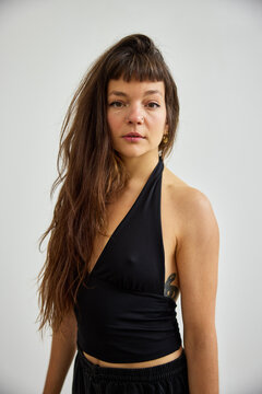 Woman with long hair stands in a studio setting making a direct look