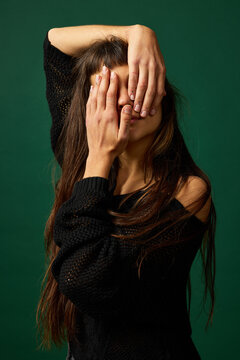 Woman covers her face with hands in front of green background