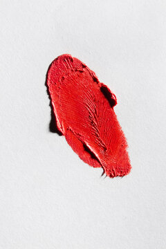 Swatch of textured red lipstick on white paper background.