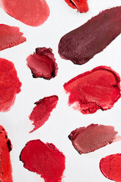 Various swatches of textured red lipsticks on white paper background.