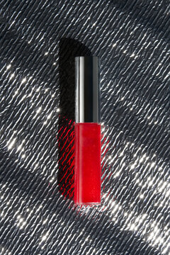Bright Red Lip Gloss on Textured Silver Surface With Light Reflections